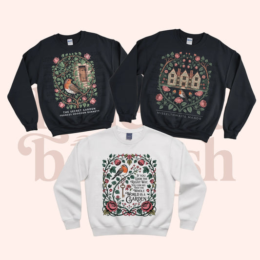 Three crewneck sweatshirts displayed together on a pale pink background: two black sweatshirts at the top with detailed garden-themed printed graphics, and one white sweatshirt at the bottom with a similar printed graphic. A 'Little Bit Bookish' watermark is visible behind the garments.